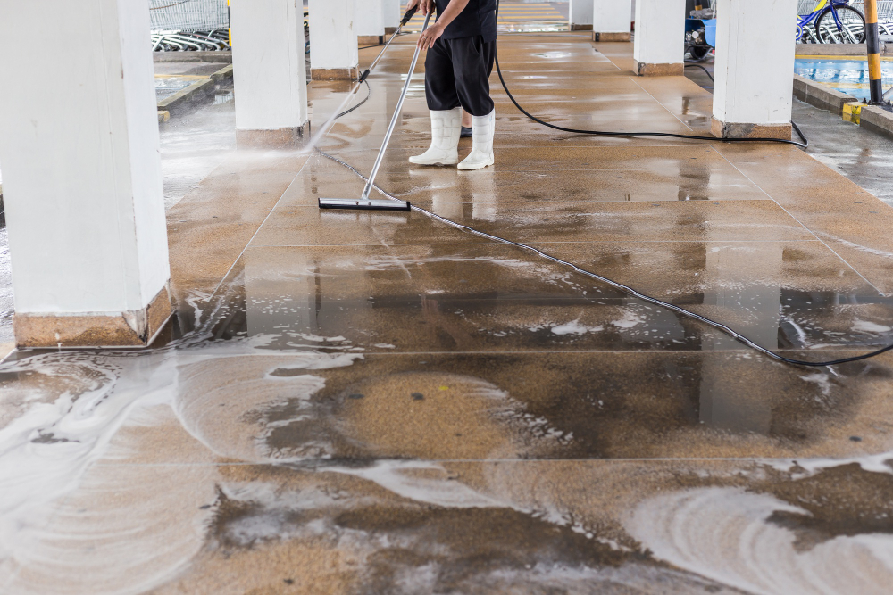 Apenas aparecendo as pernas de um homem realizando uma limpeza pós-obra com um rodo e mangueira de água.